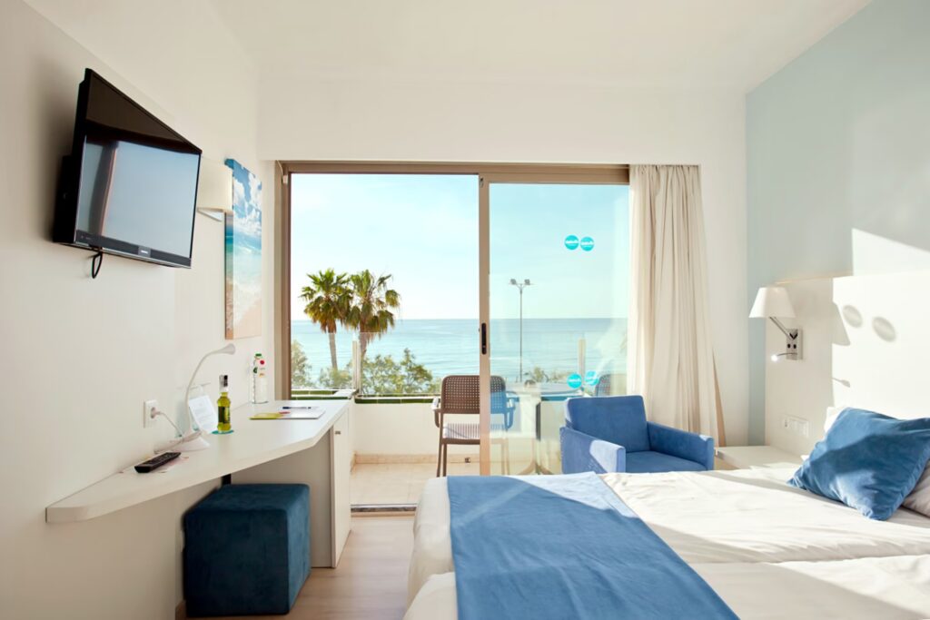 Bett mit bequemen Sessel, TV und Balkon mit Sicht auf das Meer.