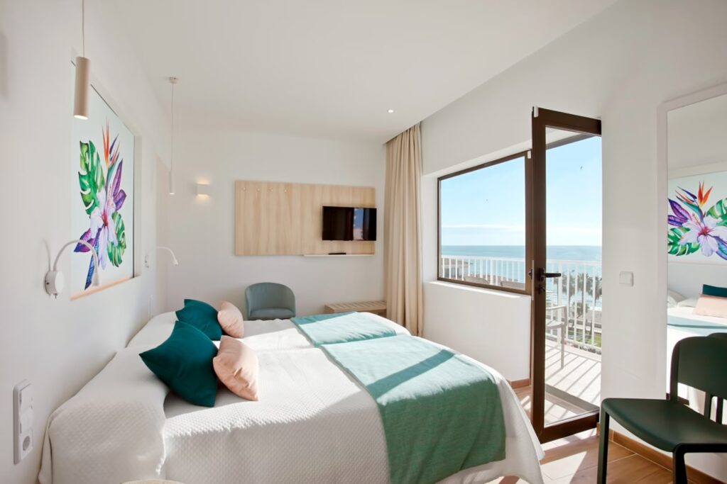 Bett mit blauen Kissen und Balkon mit Sicht auf das Meer.