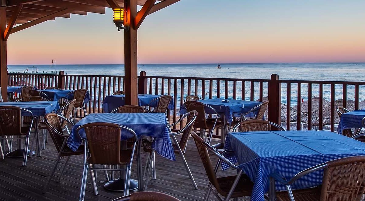 Sicht auf gedeckte Tische und Stühle und das Meer bei Abendstimmung.